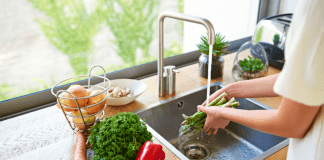 A woman washing vegetables in a kitchen sink.