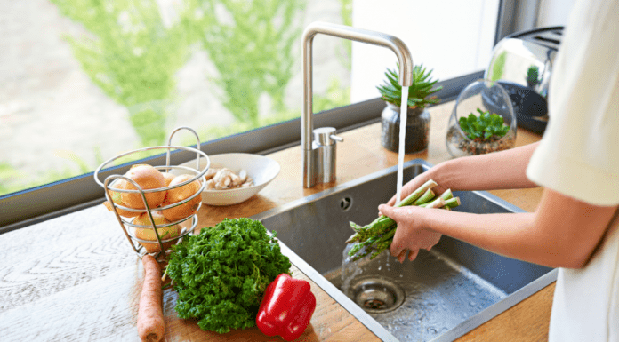 A woman washing vegetables in a kitchen sink.