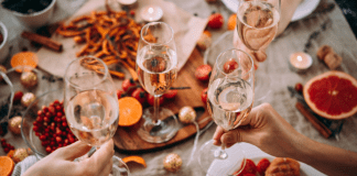 Glasses of champagne being held over a table of holiday food.