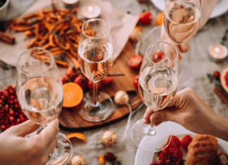 Glasses of champagne being held over a table of holiday food.