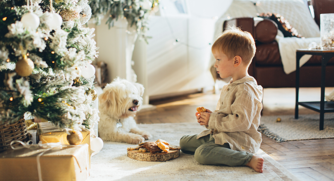 A toddler sitting by a Christmas tree. 