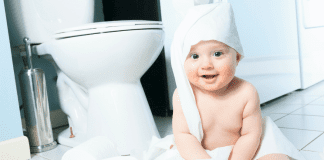 A baby wrapped in toilet paper sitting next to a toilet.