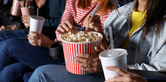 Women eating popcorn and drinking soda in a movie theatre.