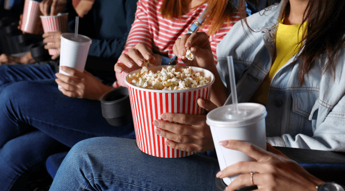 Women eating popcorn and drinking soda in a movie theatre.