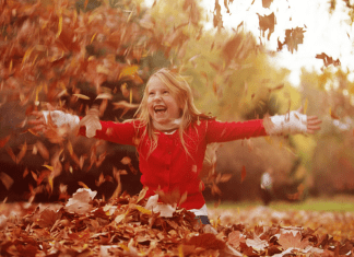 A girl playing in a pile of leaves.