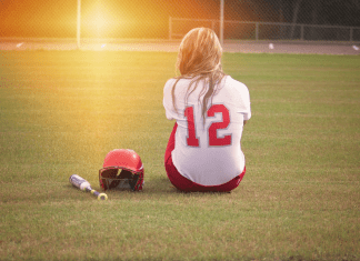 A softball player sitting in the middle of the field.