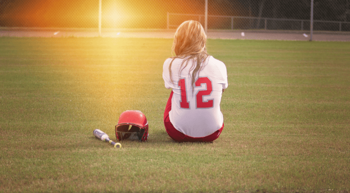 A softball player sitting in the middle of the field.