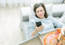 A woman on her phone eating a box of pizza.