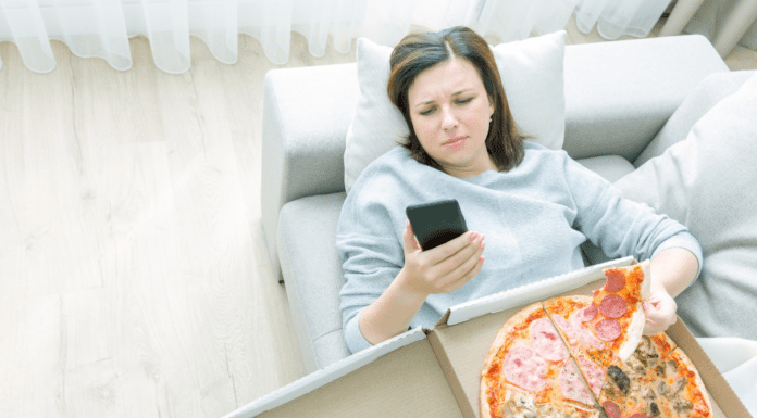 A woman on her phone eating a box of pizza.
