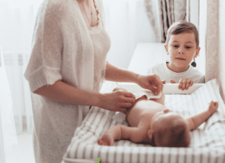 The Decision to Have a Second Baby A woman changing a baby's diaper while her toddler watches.