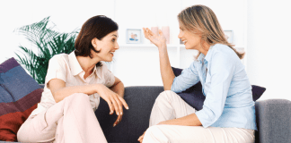 Women sitting on a couch having an exchange of words.