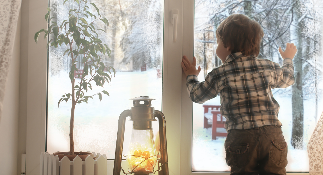 A boy looking out the window at the falling snow.