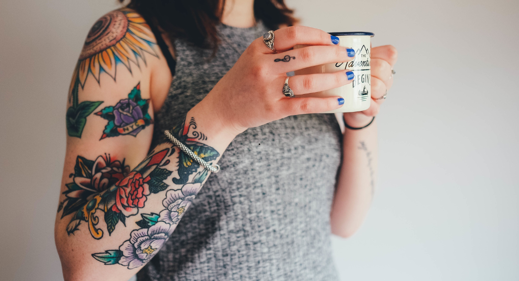 A woman with tattoos holding a coffee cup.