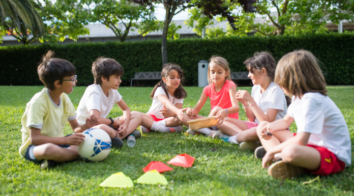 Kids sitting in a circle outside with a soccer ball.