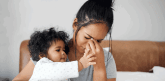 Talk To Me Tomorrow A woman holding her baby while she holds her face.