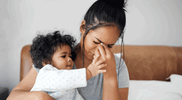 A woman holding her baby while she holds her face.