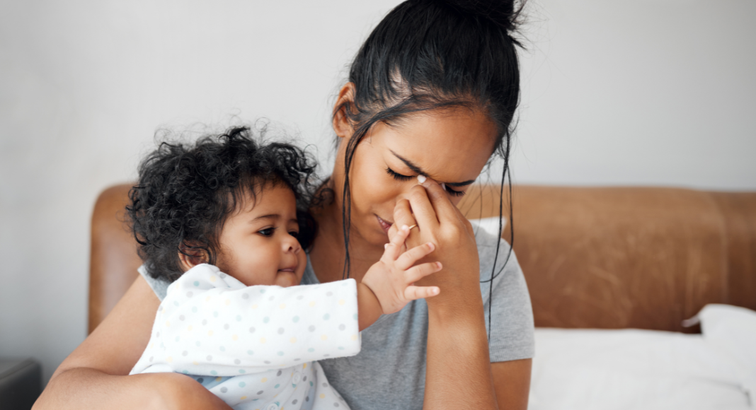 A woman holding her baby while she holds her face.