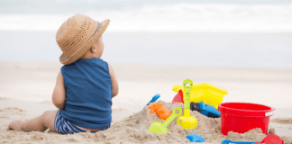 Only This Summer A baby boy sitting on the beach next to his sand toys.
