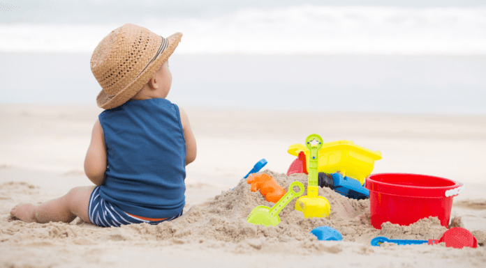 Only This Summer A baby boy sitting on the beach next to his sand toys.