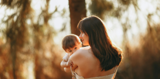 A mom holding her baby in the sunlight.