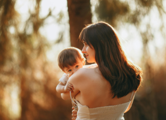 A mom holding her baby in the sunlight.
