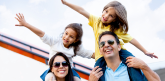 A family of four. The kids are sitting on the parent's shoulders with their arms out.