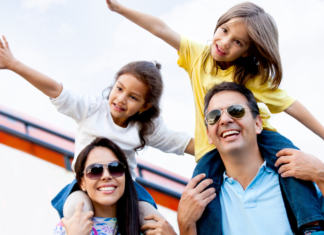 A family of four. The kids are sitting on the parent's shoulders with their arms out.
