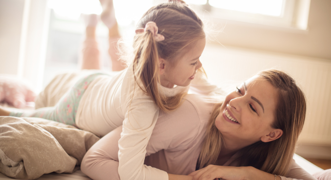 A woman laying down with her daughter on top of her smiling. 