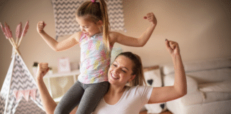 A mom holding her daughter on her shoulder making muscles.