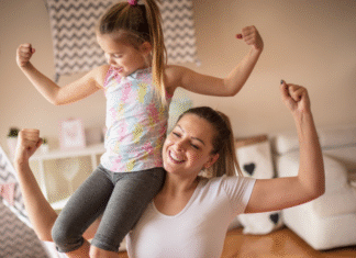 A mom holding her daughter on her shoulder making muscles.