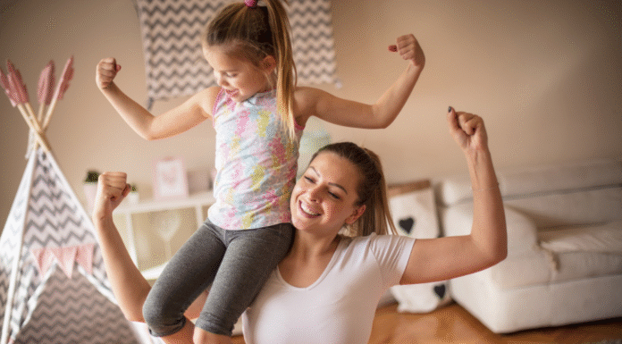 A mom holding her daughter on her shoulder making muscles.