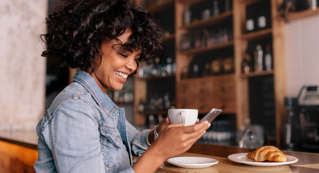 A woman reading on her phone while drinking coffee. 