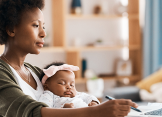 Ditch the Same Old “New Year, New Me” Speech A mom working while holding her baby.