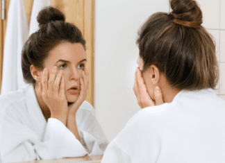 A woman looking in the mirror at her face.