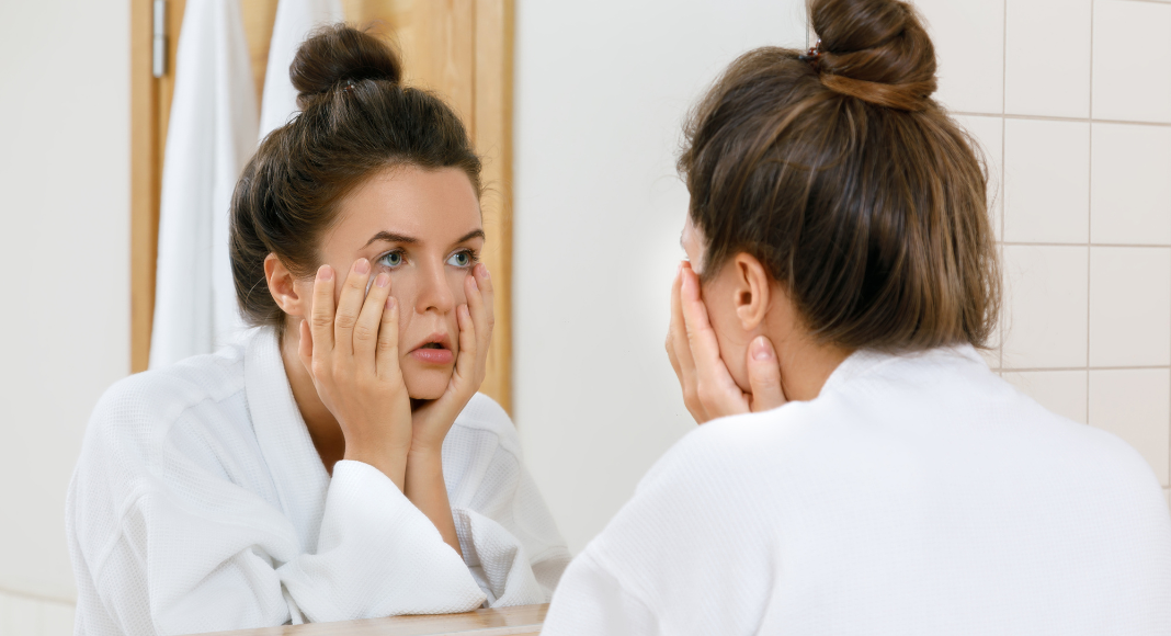 A woman looking in the mirror at her face. 