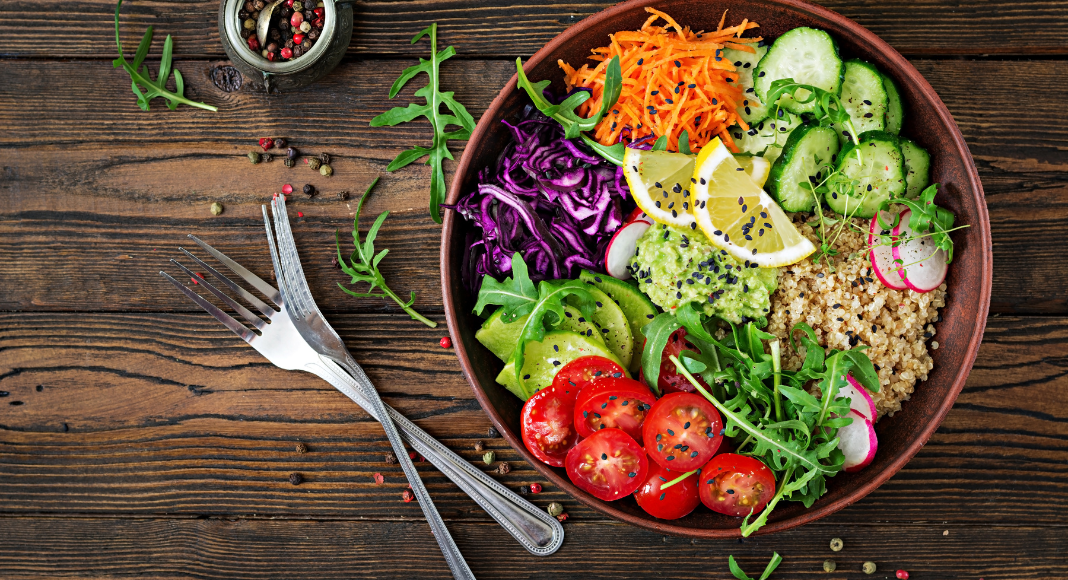 A vegetarian meal in a bowl next to a for and knife. 