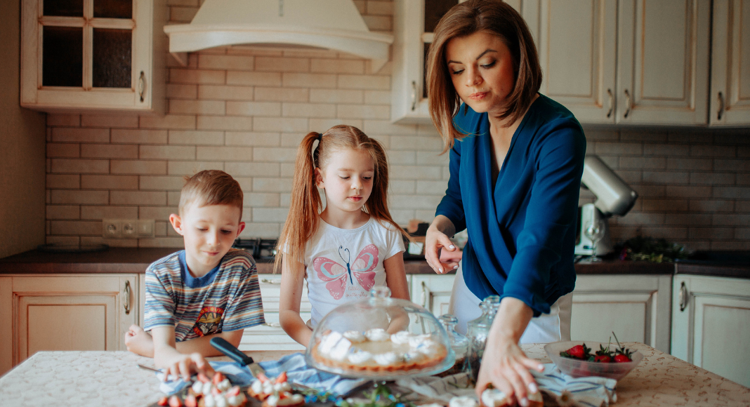 A mom and her kids looking at desserts on the counter. 