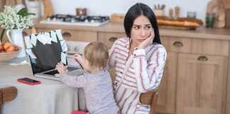 The Mom Burnout A mother sitting at the computer with a toddler in her lap.