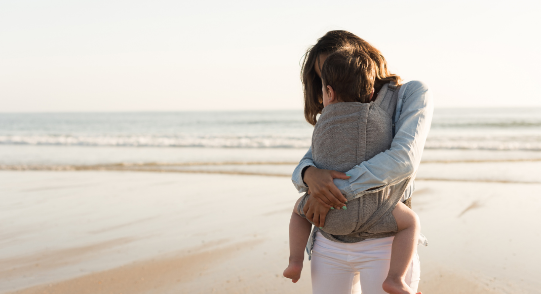 A woman holding a toddler on the beach.