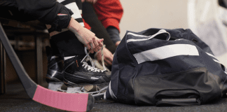 Tying up hockey skates next to a hockey bag.