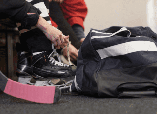Tying up hockey skates next to a hockey bag.