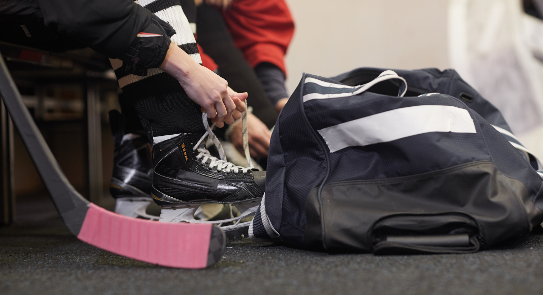 Tying up hockey skates next to a hockey bag.
