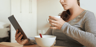 A woman reading the news while eating breakfast.
