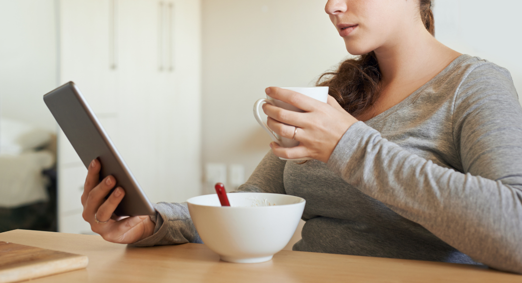 A woman reading the news while eating breakfast.