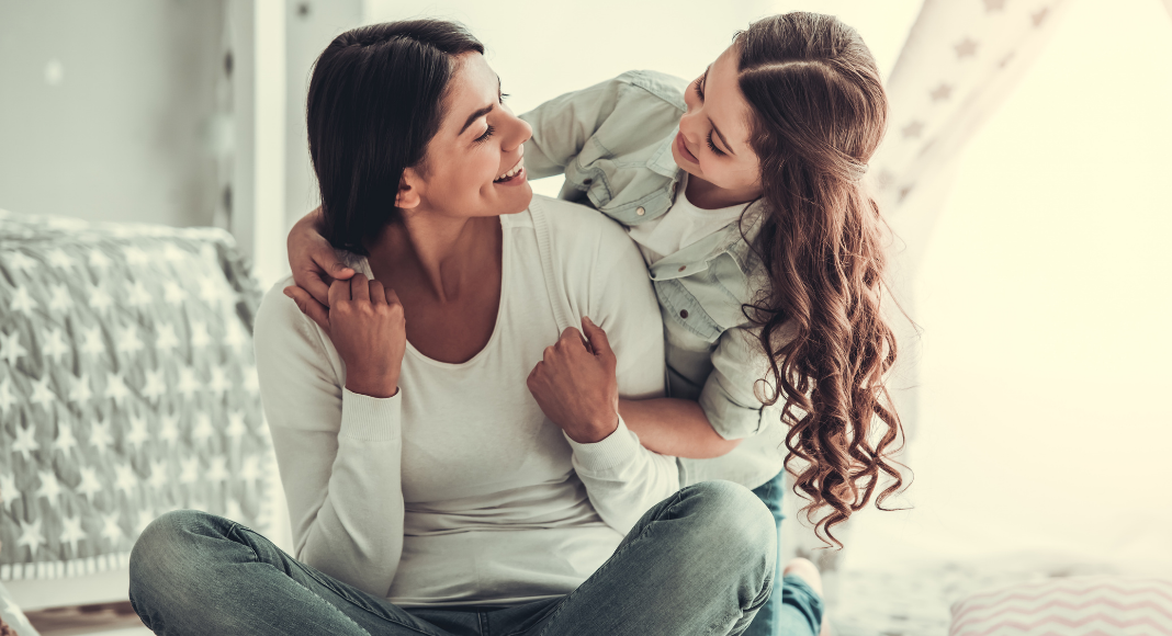 A girl hugging her mom from behind. 