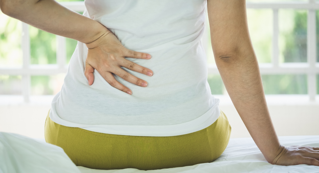 A woman sitting holding her back.
