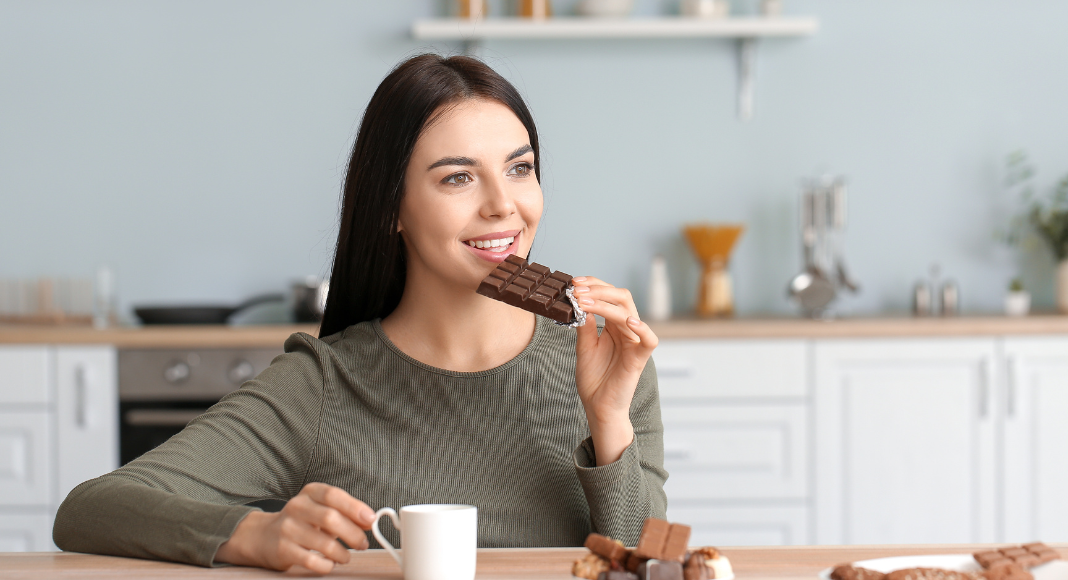 A woman eating chocolate and drinking coffee.