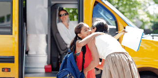 A mom hugging her daughter before she gets on the school bus.