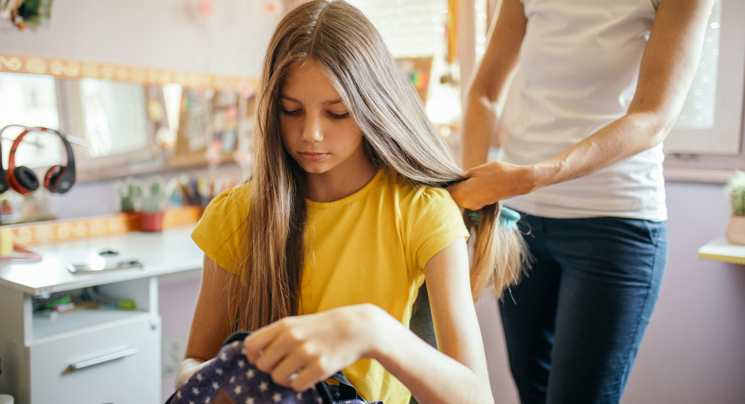 A mom brushing her daughter's hair while getting ready for school.