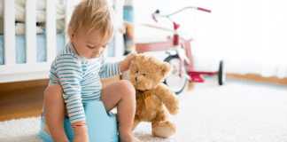 A boy sitting on a potty holding his teddy bear.